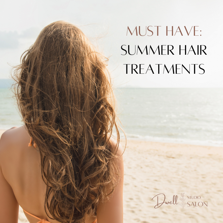 Woman with long, wavy blonde hair seen from behind on a sunny sandy beach, with text overlay reading "Must Have: Summer Hair Treatments" by Dwell Studio Salon.
