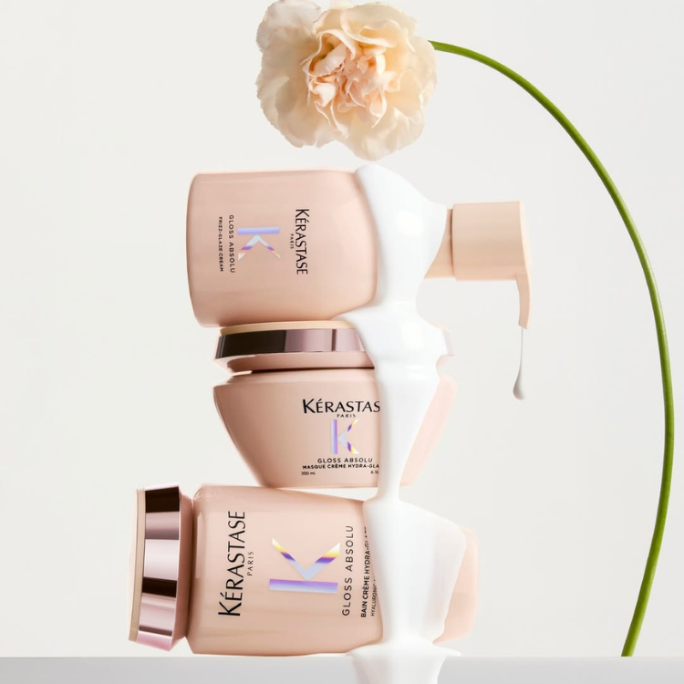 Kérastase Gloss Absolu luxury hair products stacked with white cream dripping down the side next to a single carnation