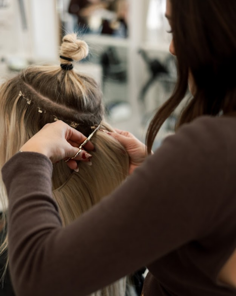 Stylist installing hand-tied hair extensions into a client's sectioned blonde hair
