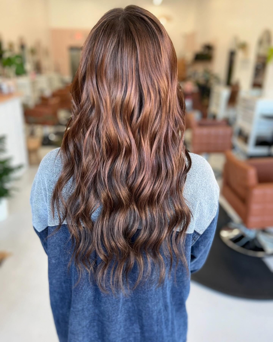 Back view of long wavy warm brown hair styled after hand-tied extension installation by Ashley.