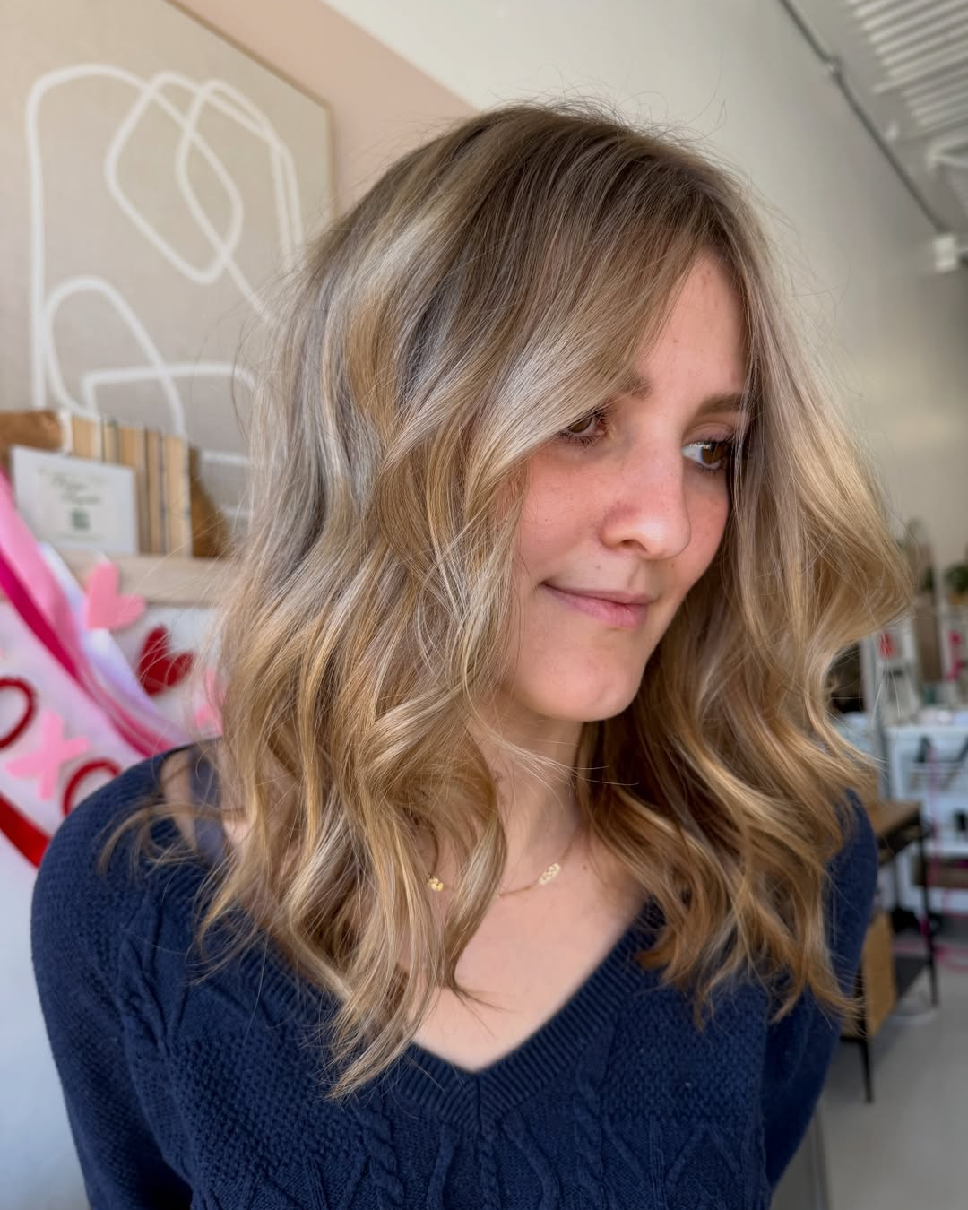 Woman with shoulder-length wavy blended blonde hair and subtle curtain bangs.