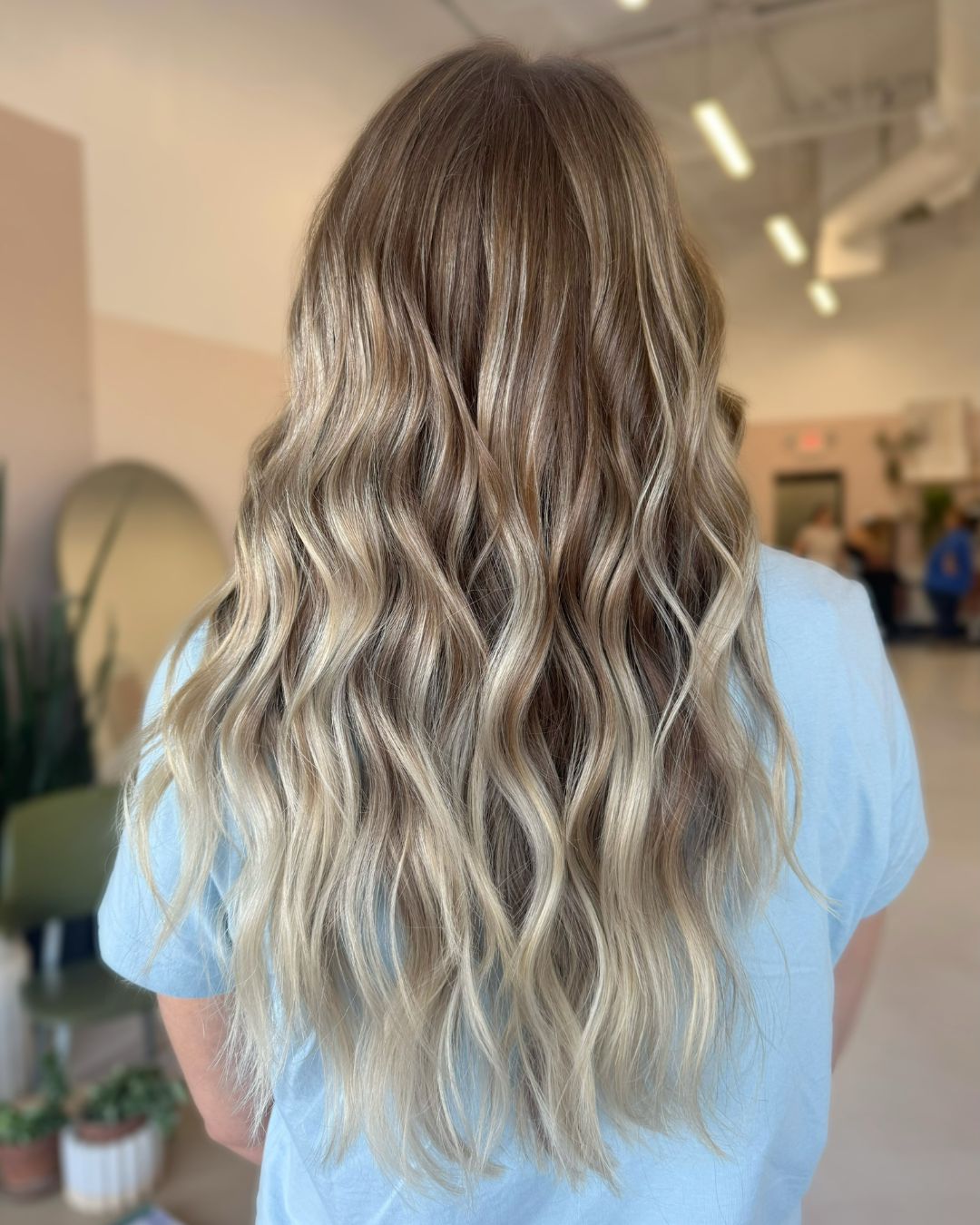 Back view of long, dimensional blonde balayage hair with soft, cascading waves by Zoe.