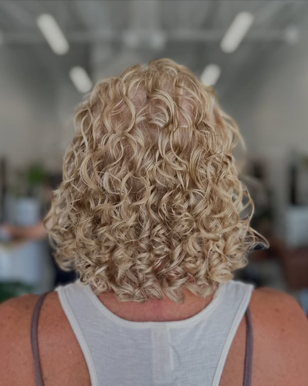 Back view of short blonde curly haircut with natural curl definition by Abigail.