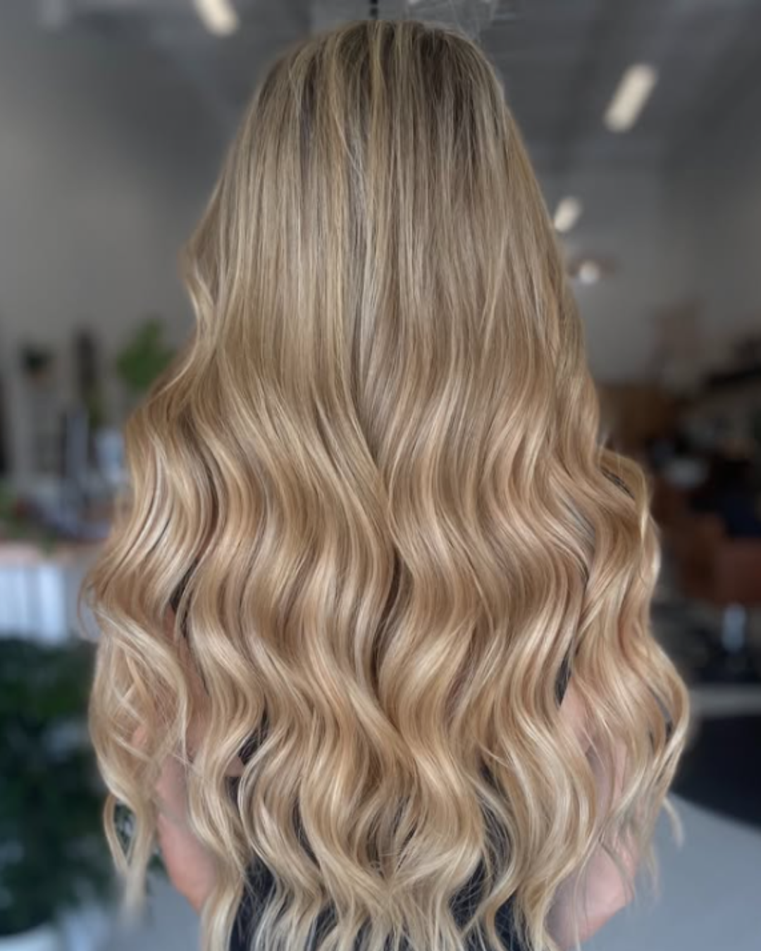 Back view of long, dimensional blonde hair with extensions styled in soft, cascading waves.