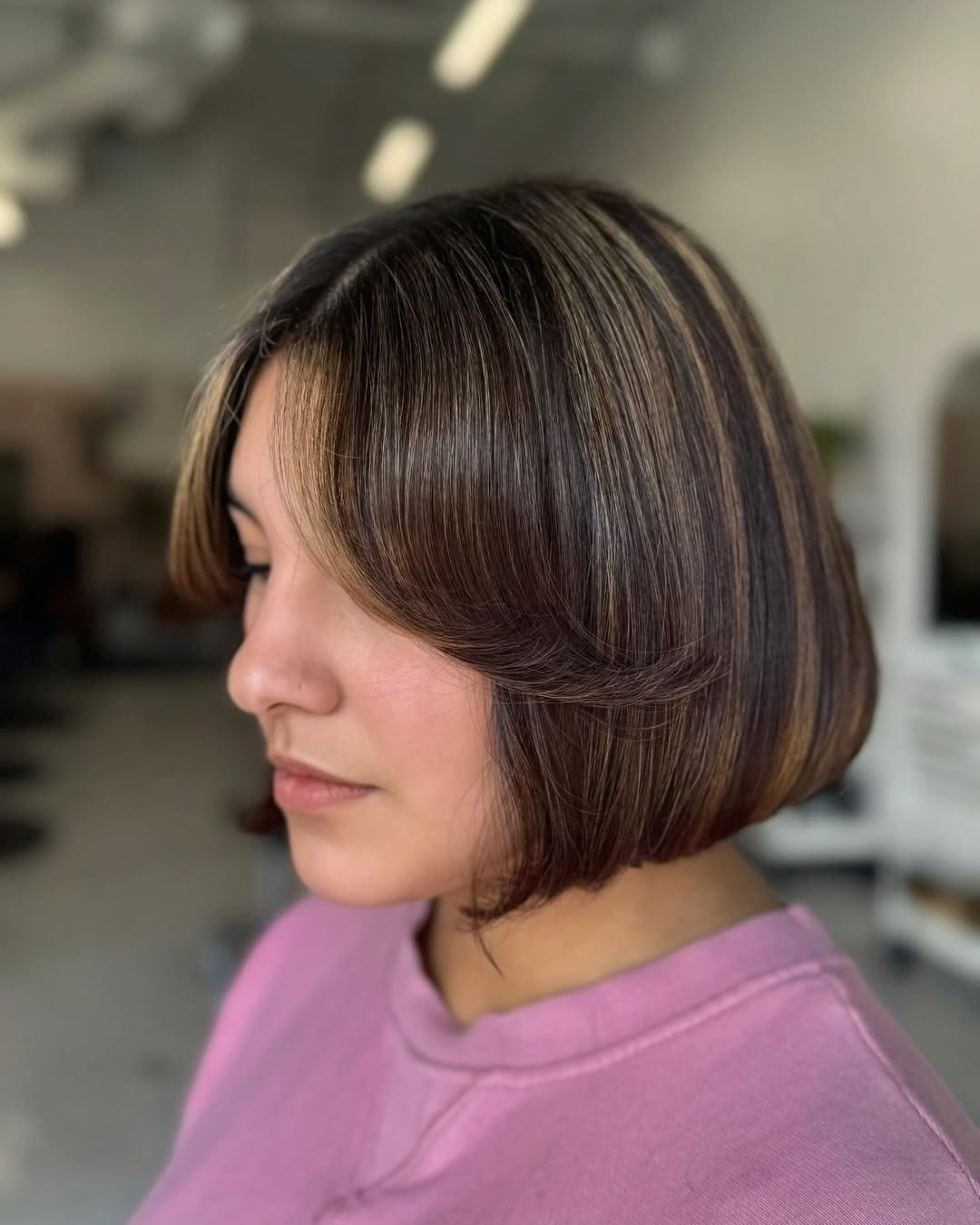 Side profile of a short dark brown bob haircut featuring caramel highlights and voluminous curtain bangs by Zoe.