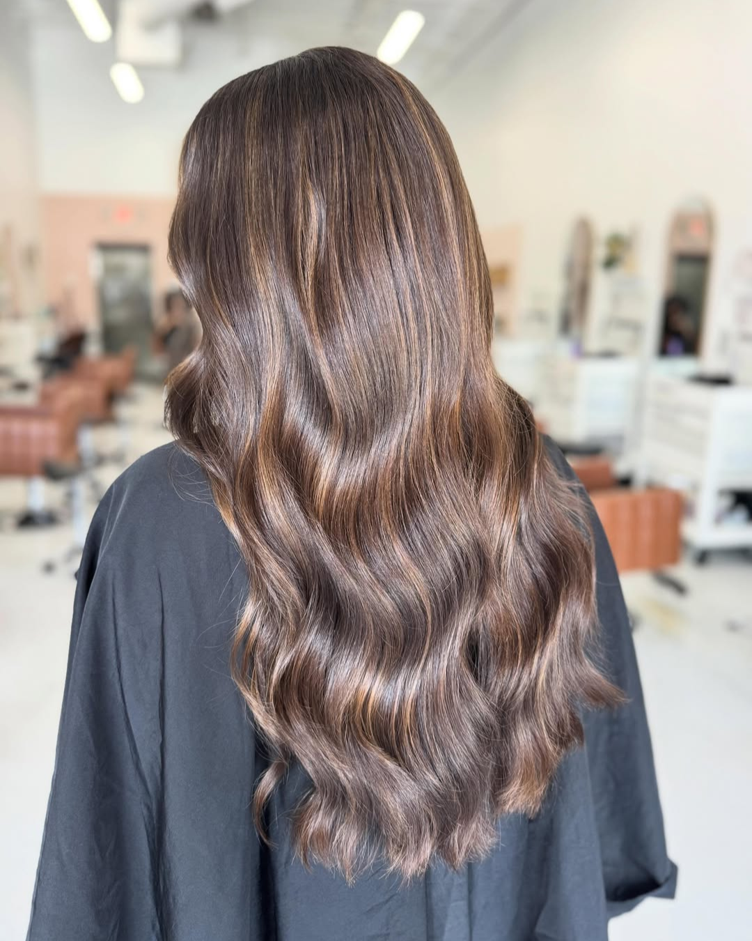 Back view of long dark brown hair styled with soft waves and caramel ribbon highlights.