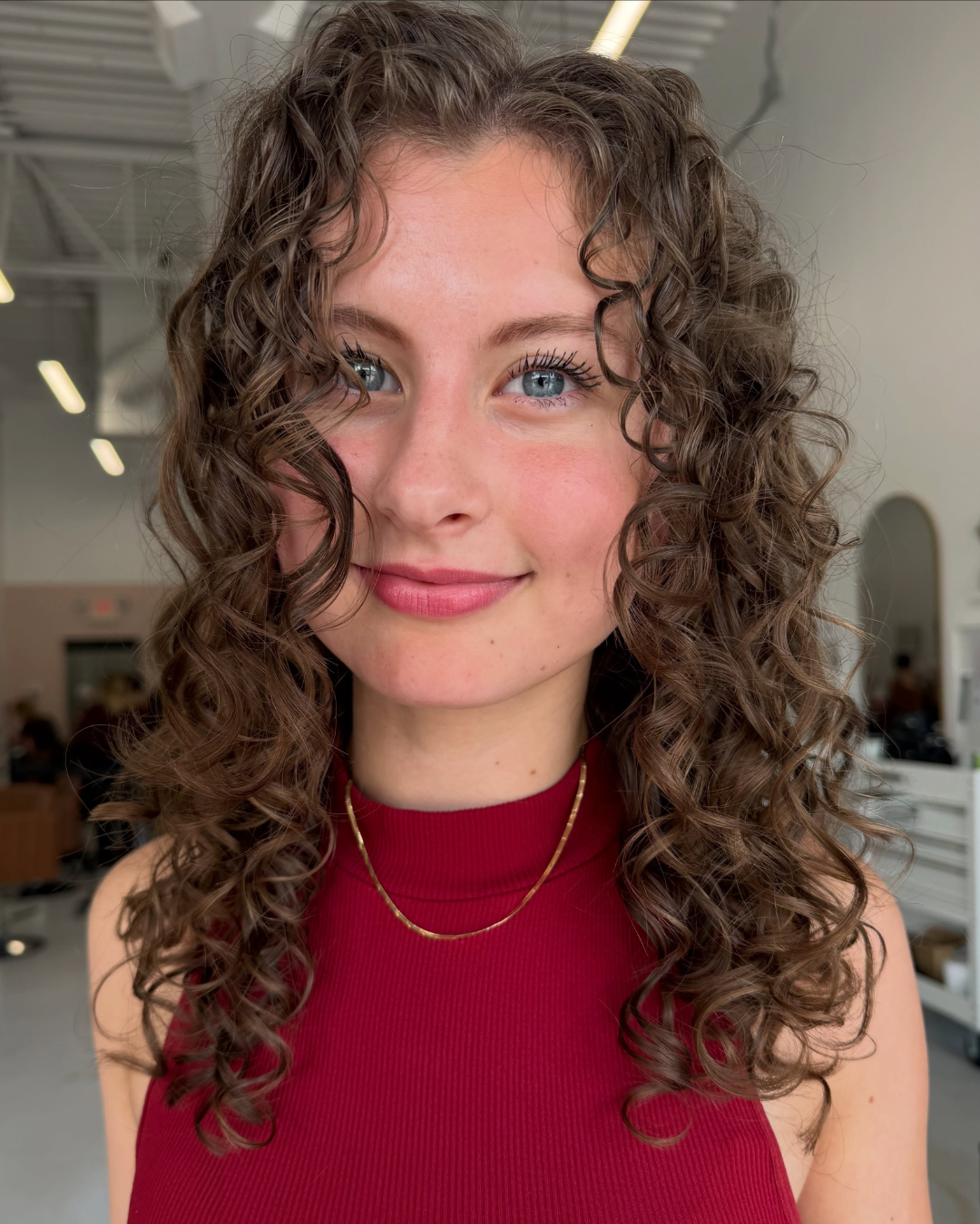 Close-up portrait of woman with defined brown curly haircut styling by Abigail.