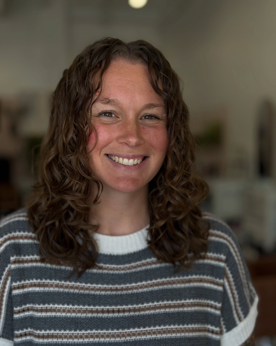 Smiling woman with medium-length defined brown curly hair and curtain curls by Angela.