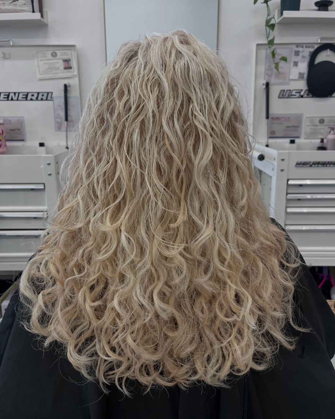 Back view of long platinum blonde hair styled in soft natural curls and waves by Ashley.