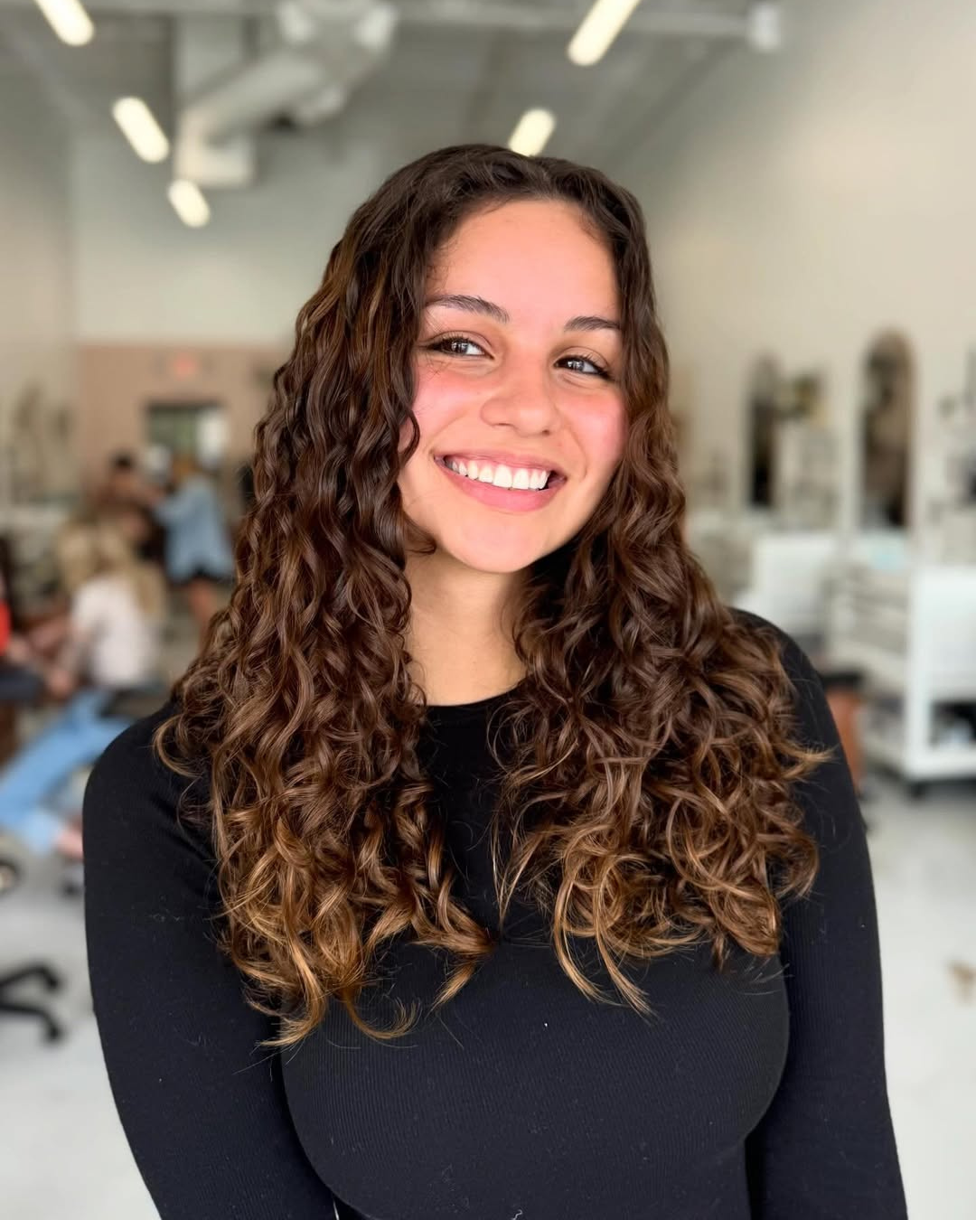 Smiling woman with long, layered brown curly hair styled with soft ringlets.