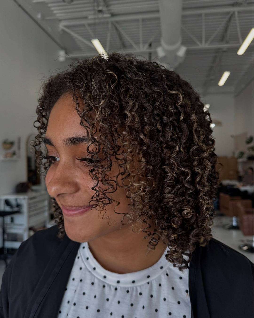 Side profile of a woman with medium-length, dark brown curly hair and defined ringlets.