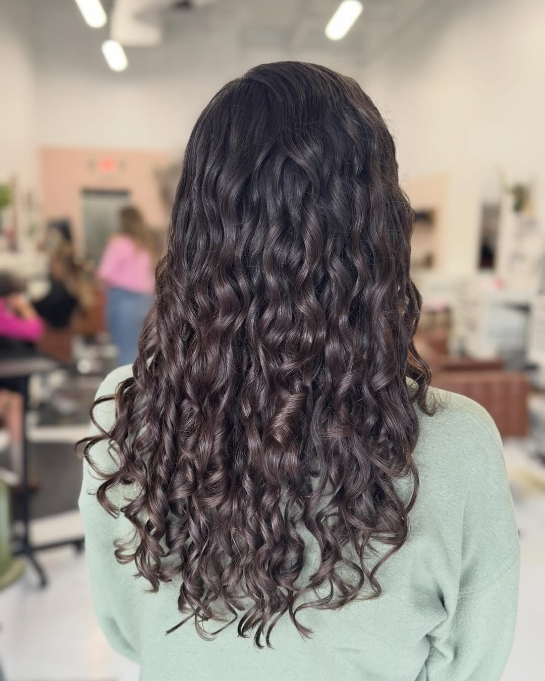 Back view of a person with long, dark brown curly hair styled with defined ringlets.