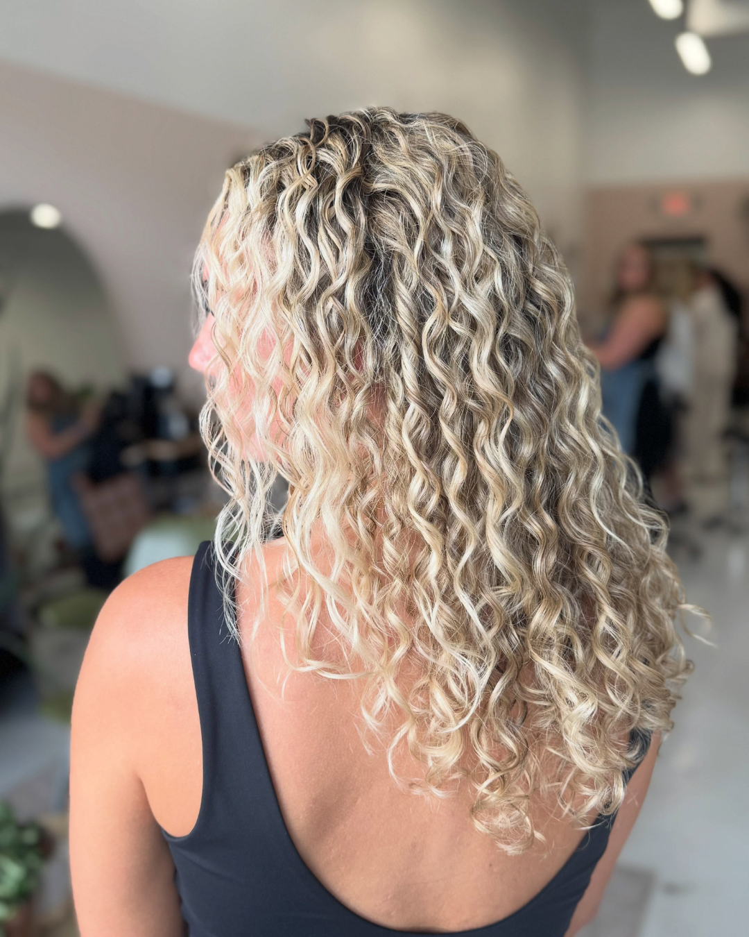 Side view of long, curly blonde-highlighted hair with defined ringlets and layered volume by Zoe.