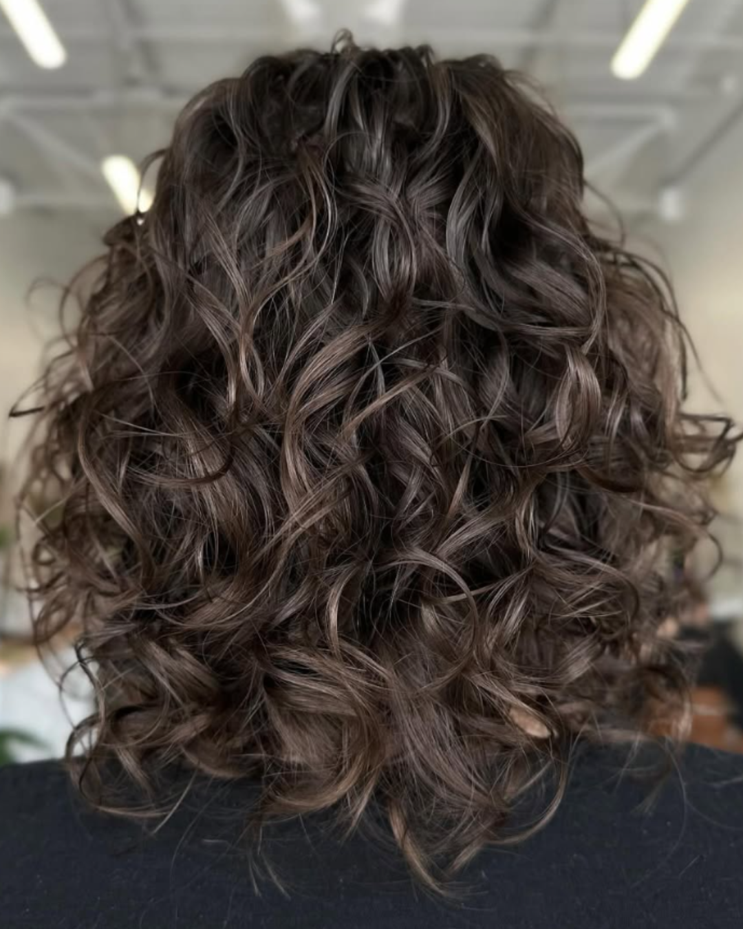 Medium-length brown curly haircut styled with defined ringlets by Abigail.