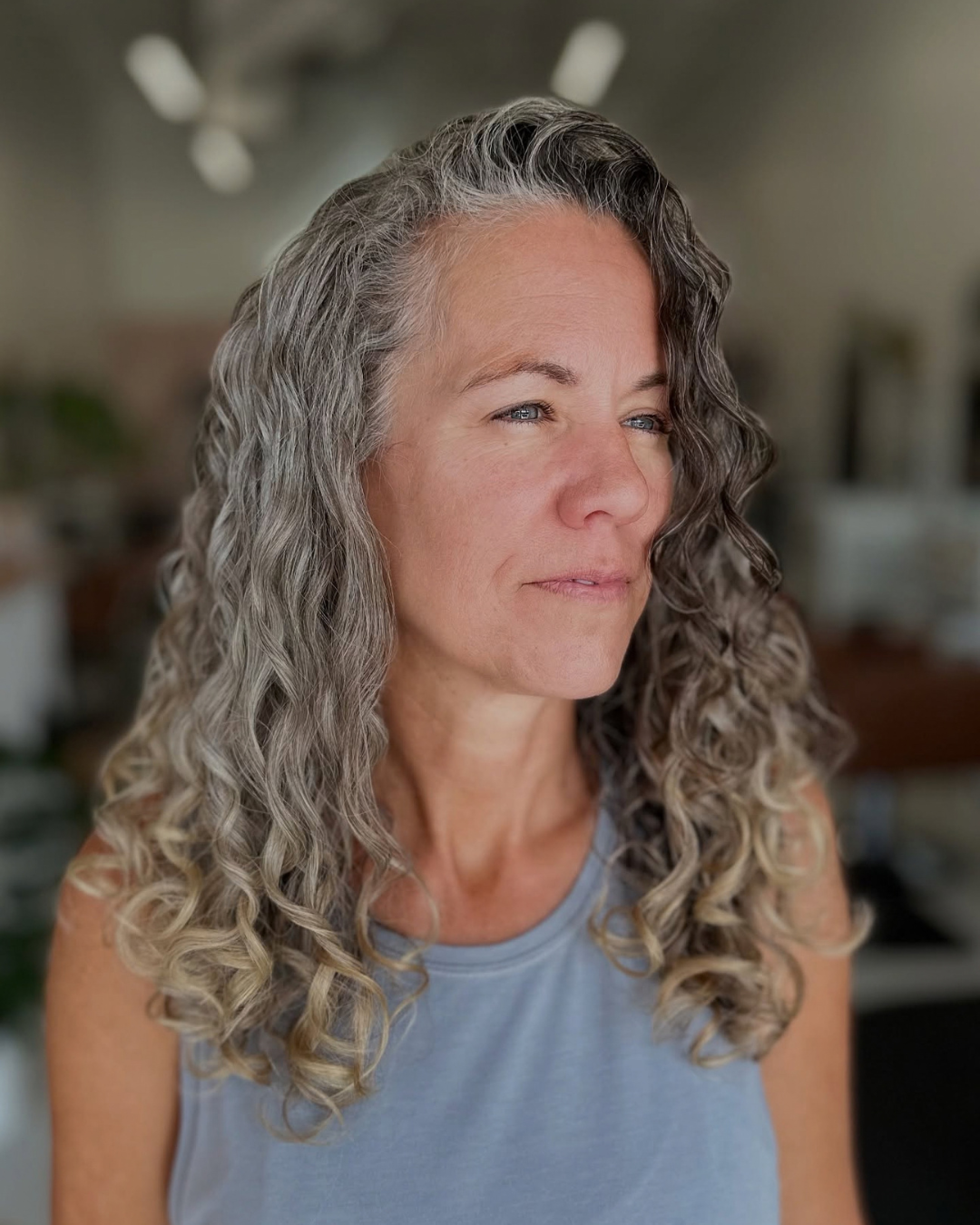 Woman with long, dry-cut natural gray and silver curly hair posing for a portrait.