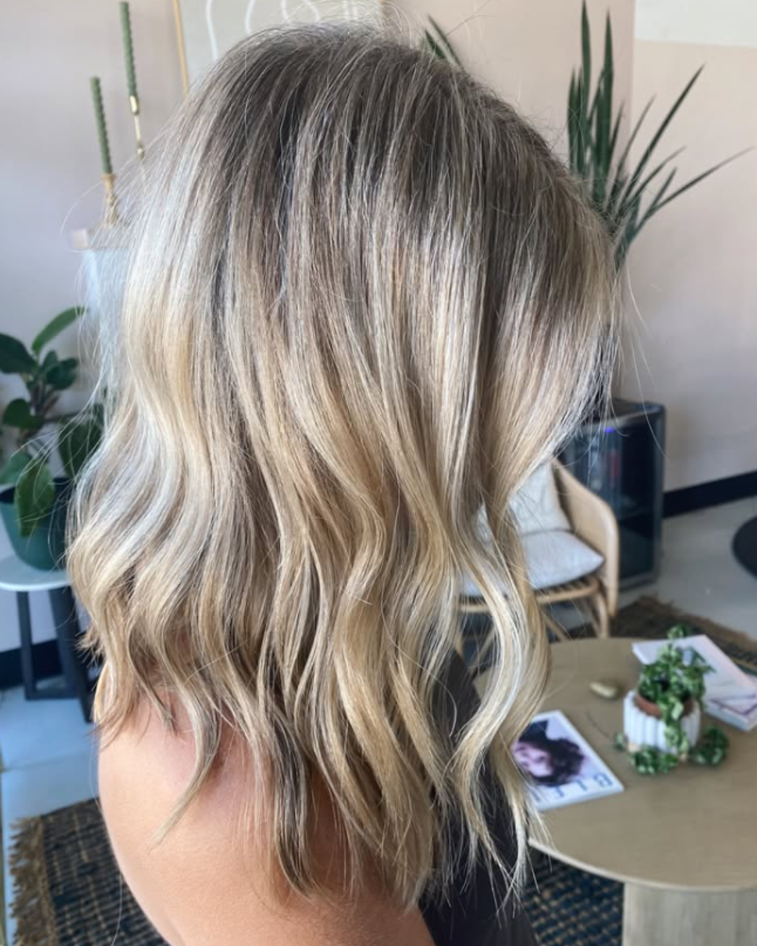 Side view of a medium-length lived-in blonde hairstyle with dark roots and soft, textured waves.