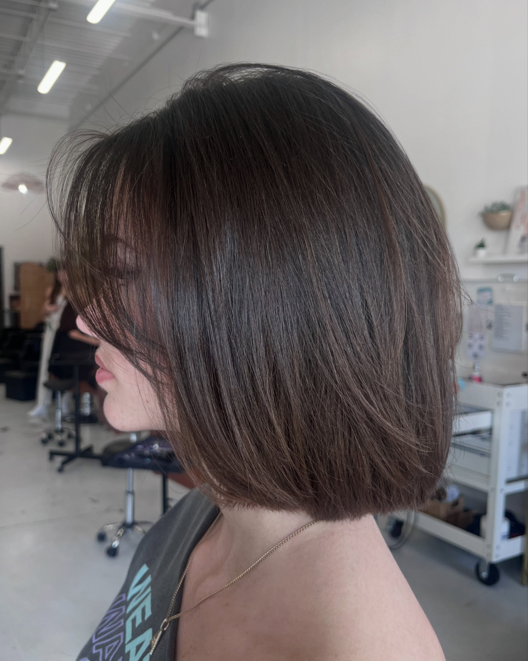 Side view of a dark brown sleek long bob haircut with soft curtain bangs by Ashley.