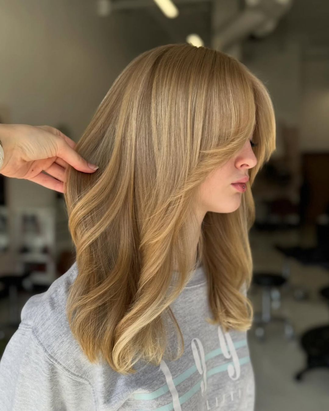 Side profile of long blonde hair with soft, voluminous layers and face-framing curtain bangs by Zoe
